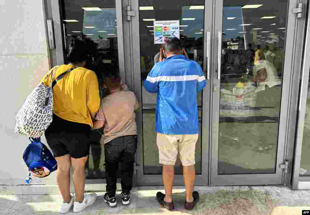 Cubanos miran a través de los cristales del nuevo supermercado en dólares inaugurado en La Habana.