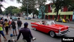 Turistas se pasean en un almendrón mientras varias personas esperan por el transporte público en una parada en La Habana. (Reuters/Alexandre Meneghini)